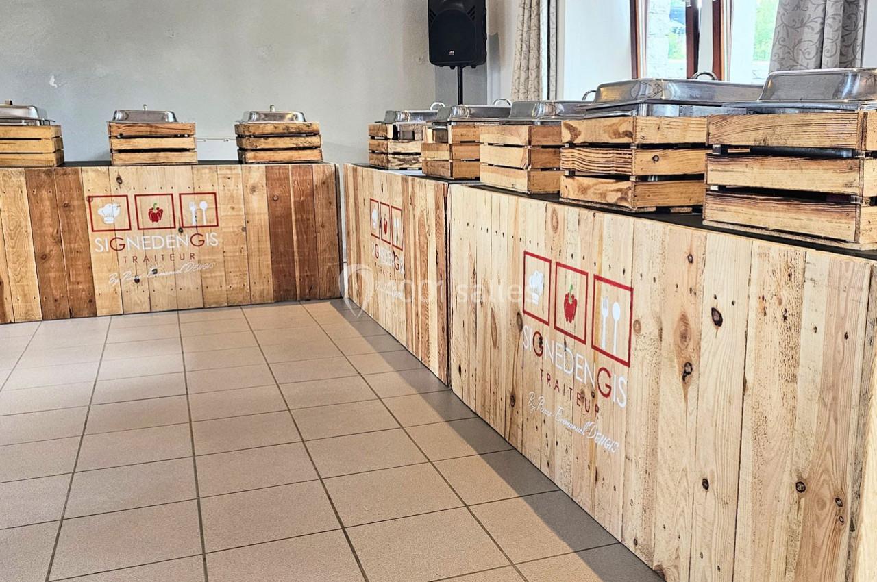 Buffet en bois avec des plats en inox disposés sur des caissons, dans une salle lumineuse avec carrelage au sol.