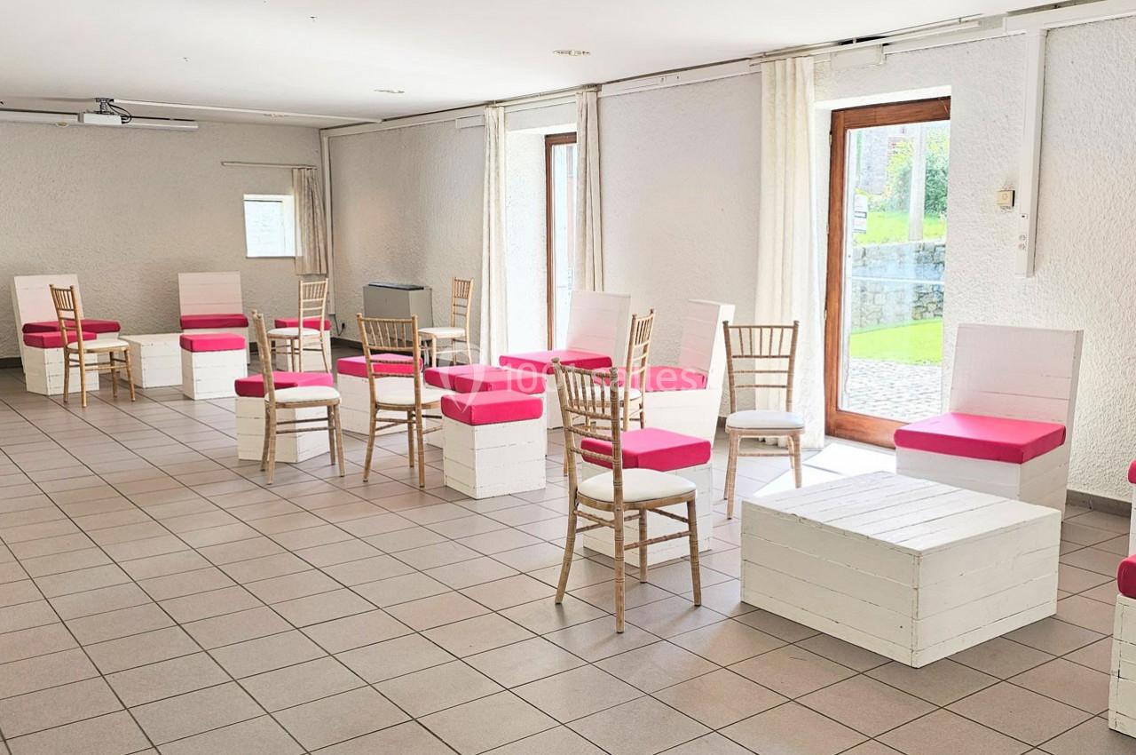 Salle lumineuse avec des chaises en bois et des bancs blancs aux coussins roses, disposés sur un sol carrelé.