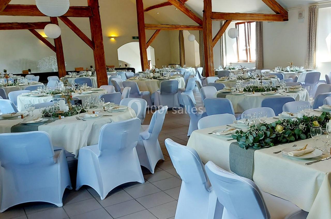 Salle de réception décorée avec des tables rondes dressées, nappes blanches et chaises couvertes, ambiance lumineuse.