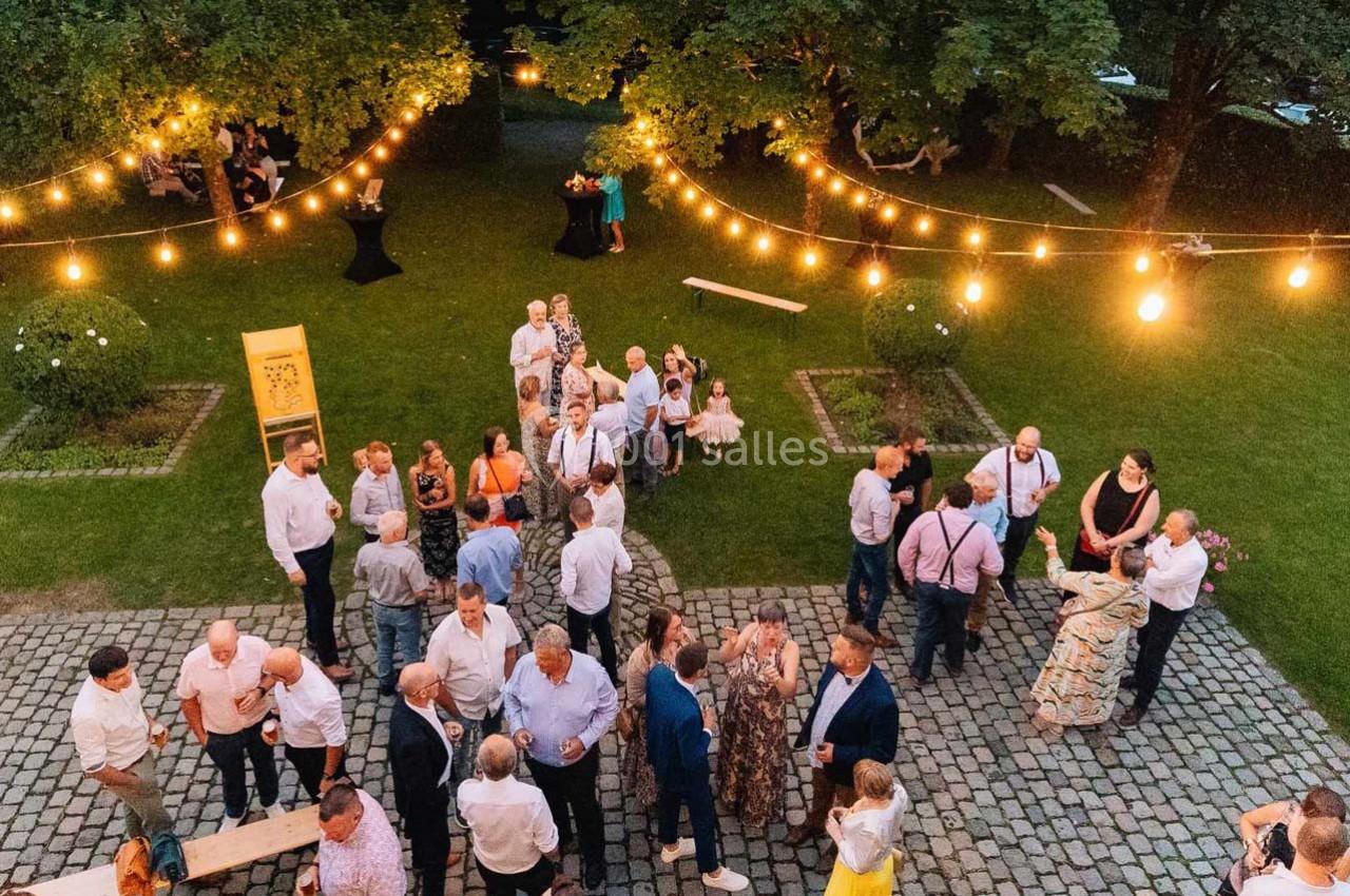 Groupe de personnes discutant dans un jardin éclairé par des guirlandes lumineuses en soirée.