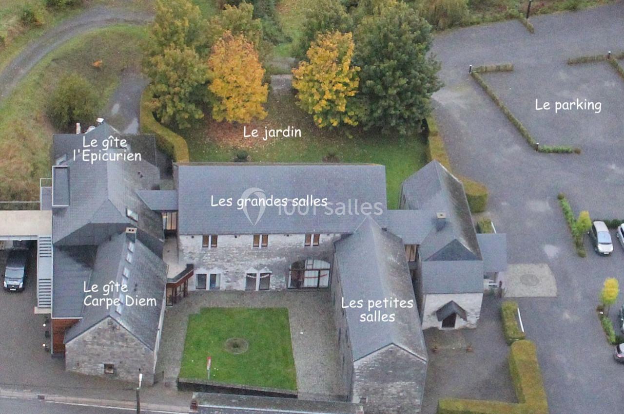 Vue aérienne d'un complexe avec plusieurs bâtiments, un jardin central, un parking et des zones identifiées par des noms.