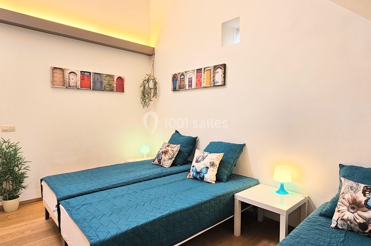 Deux lits simples avec couvre-lits bleus, tables de chevet blanches et décorations murales colorées dans une chambre…