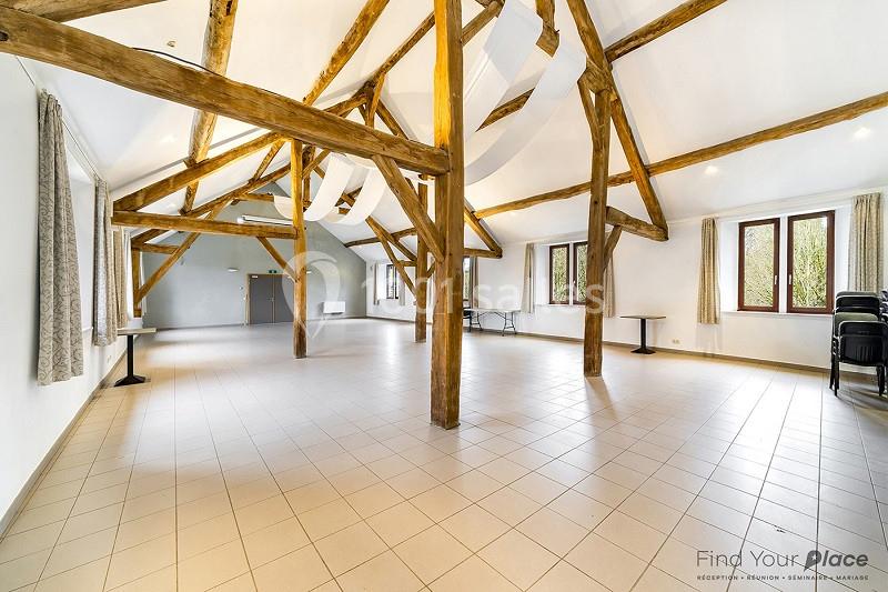 Salle lumineuse avec poutres apparentes, carrelage clair, grandes fenêtres et rideaux, aménagée pour des événements.