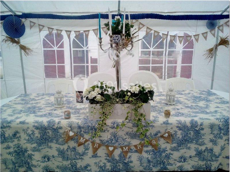 Table décorée pour un mariage sous une tente, avec nappe bleue et blanche, guirlandes, fleurs et bougies.