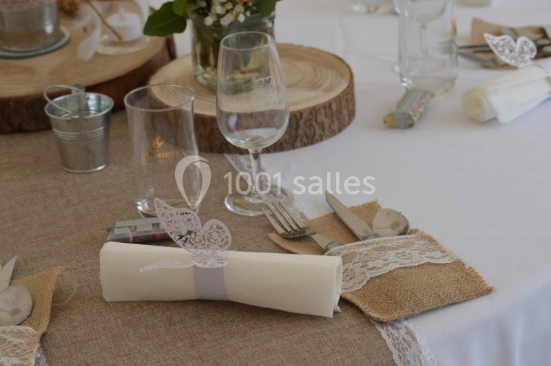 Table décorée avec nappe en lin, rondins de bois, serviettes ornées de dentelle et papillons en papier.