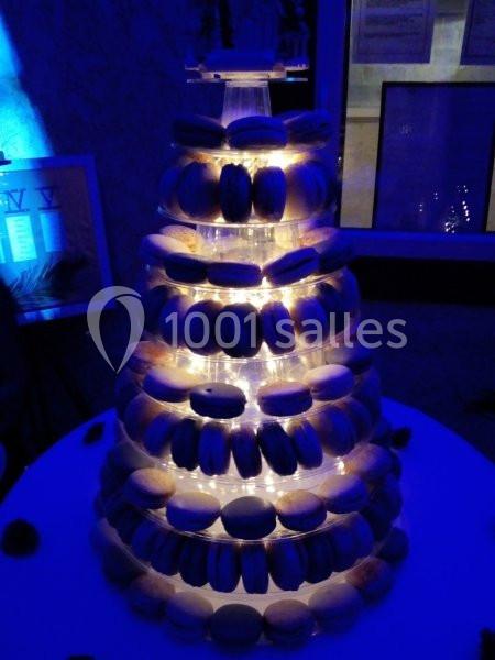 Tour de macarons éclairée sur une table ronde dans un environnement sombre.