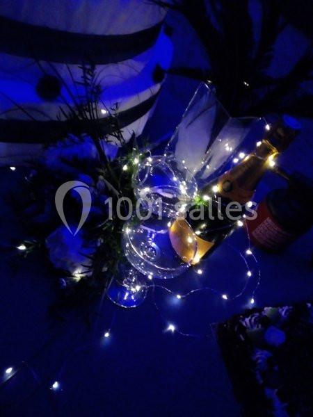 Bouteille de champagne, flûtes et décorations lumineuses sur une table dans une ambiance tamisée bleutée.