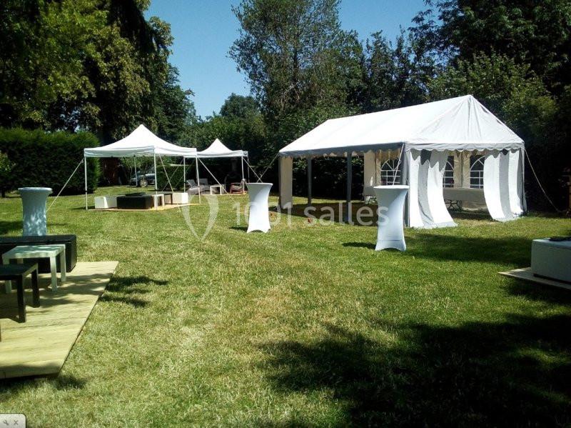 Tentes blanches installées sur une pelouse pour un événement en extérieur, entourées d'arbres et de mobilier.