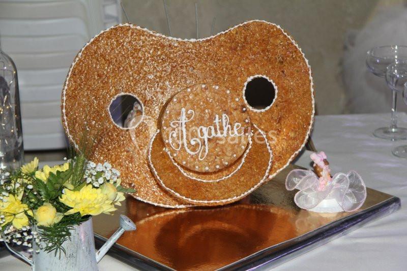 Pièce montée en forme de tétine avec le prénom ’Agathe’, décorée de perles de sucre, posée sur une table festive.