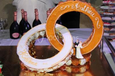 Pièce montée en forme d'anneaux entrelacés avec des figurines de mariés, entourée de bouteilles de champagne.