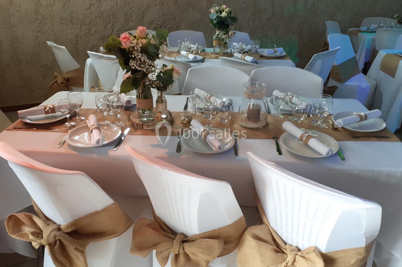Table décorée pour un événement avec nappes blanches, chaises ornées de rubans en toile de jute et centre de table floral.