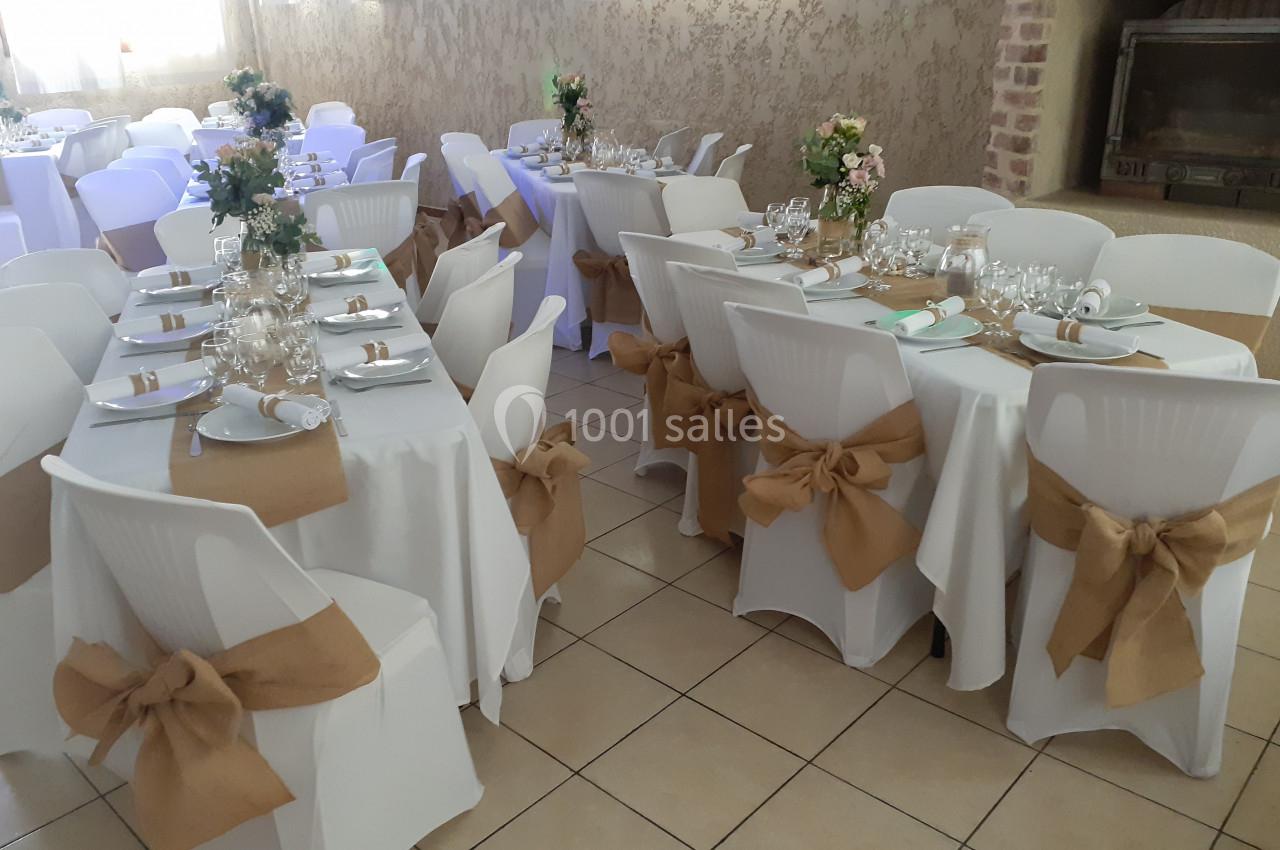 Salle de réception décorée avec des tables dressées, nappes blanches et chaises ornées de nœuds en toile de jute.