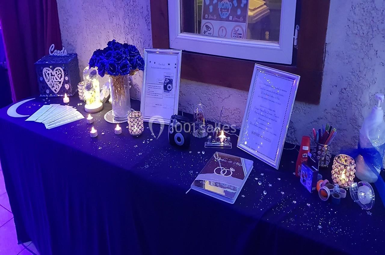 Table décorée pour un événement avec bougies, fleurs, cadres, accessoires photo et livre d'or sur une nappe sombre.