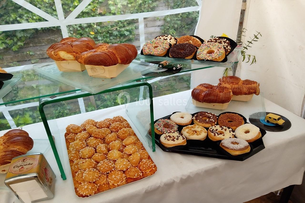 Présentation de viennoiseries, donuts et pâtisseries variées sur des plateaux dans un espace lumineux avec vue sur un jardin.