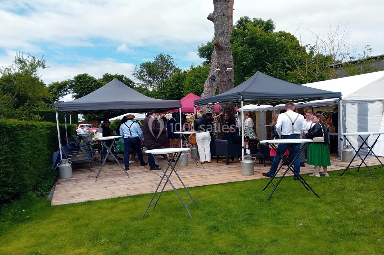 Personnes rassemblées sous des tonnelles dans un jardin, discutant autour de tables hautes lors d'un événement en plein air.