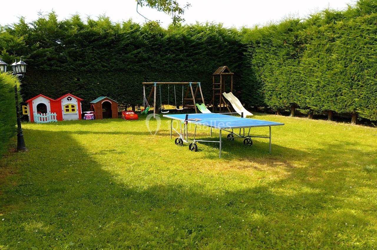 Jardin avec table de ping-pong, balançoire, toboggan et petites maisons colorées entourées de haies.