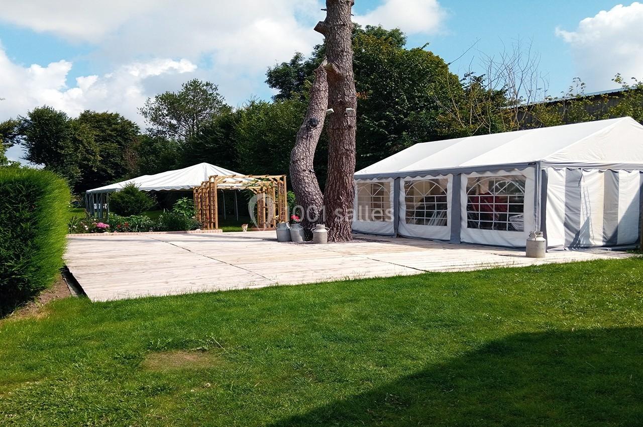 Deux tentes blanches installées sur une terrasse en bois dans un jardin verdoyant avec arbres et ciel dégagé.