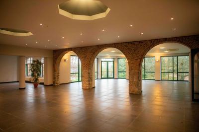 Salle vide avec de grandes baies vitrées donnant sur un espace vert, éclairée par une lumière douce.