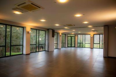 Salle vide avec de grandes baies vitrées donnant sur un espace vert, éclairée par une lumière douce.