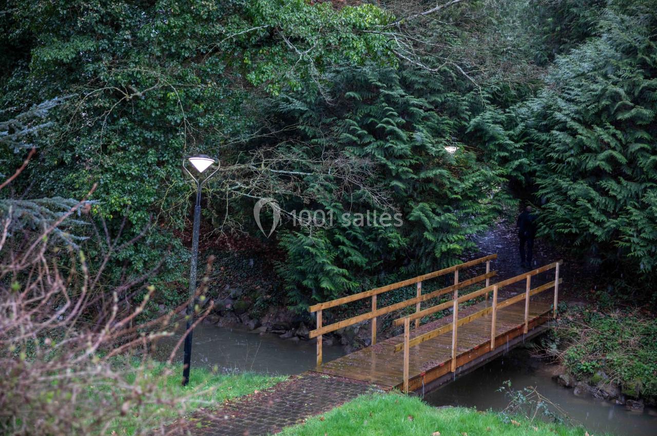 Passerelle en bois traversant un ruisseau, entourée de végétation dense et éclairée par des lampadaires.