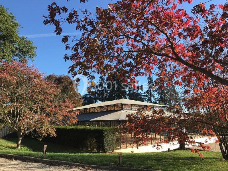 Un bâtiment vitré entouré d'arbres aux feuilles rouges et vertes sous un ciel bleu clair.