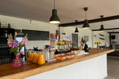 Vue d'une rivière bordée de végétation avec une maison au toit rouge et un ciel partiellement nuageux au coucher du soleil.