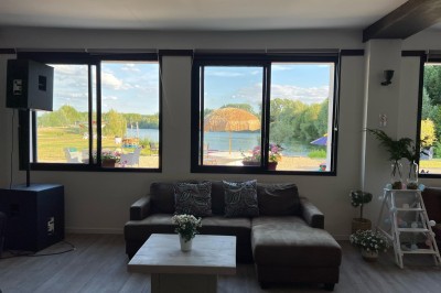 Vue d'une rivière bordée de végétation avec une maison au toit rouge et un ciel partiellement nuageux au coucher du soleil.