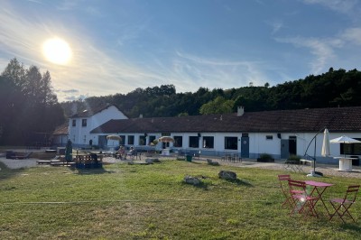 Vue d'une rivière bordée de végétation avec une maison au toit rouge et un ciel partiellement nuageux au coucher du soleil.