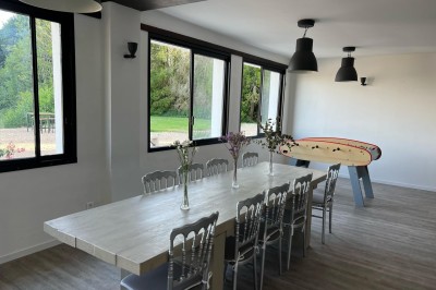 Vue d'une rivière bordée de végétation avec une maison au toit rouge et un ciel partiellement nuageux au coucher du soleil.