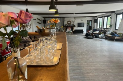 Vue d'une rivière bordée de végétation avec une maison au toit rouge et un ciel partiellement nuageux au coucher du soleil.