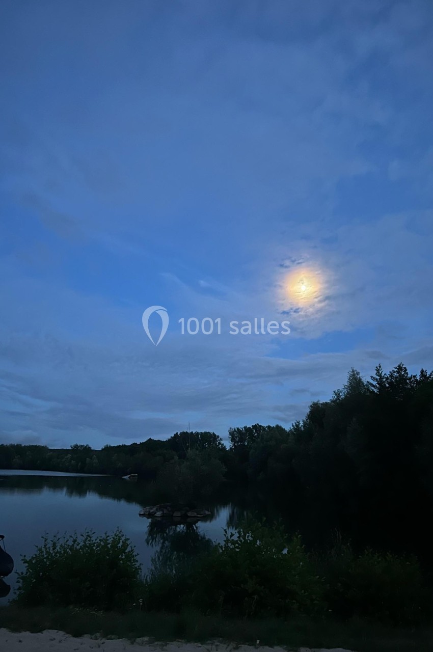 Paysage nocturne avec une rivière bordée de végétation, sous un ciel nuageux éclairé par la lune.