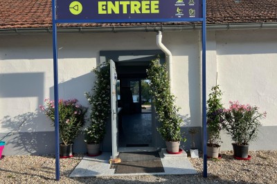 Vue d'une rivière bordée de végétation avec une maison au toit rouge et un ciel partiellement nuageux au coucher du soleil.