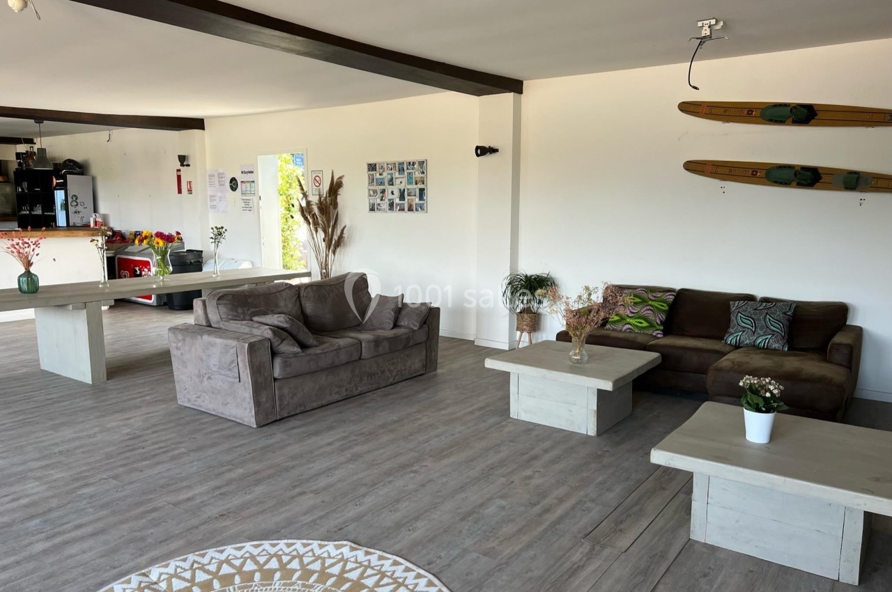 Salon lumineux avec parquet, canapés marron, tables basses blanches, skis accrochés au mur et décoration végétale.