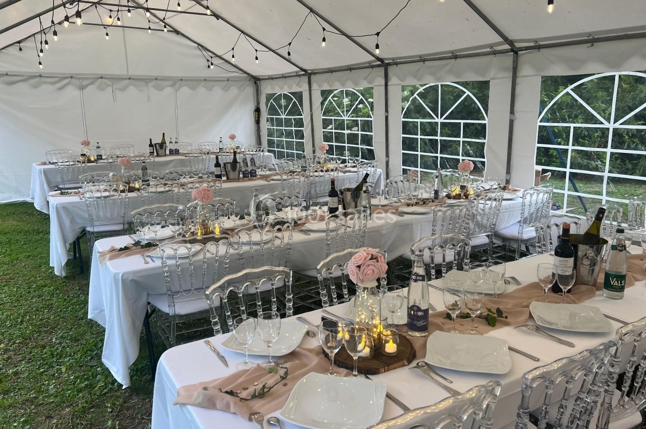 Tables élégamment dressées sous une tente blanche, décorées de roses et guirlandes lumineuses, pour un événement en plein…