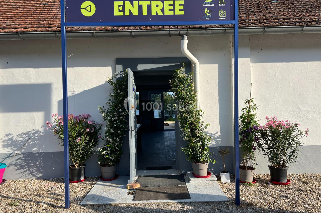 Entrée d'un bâtiment avec porte ouverte, encadrée de plantes en pots et signalée par un panneau ’Entrée’.