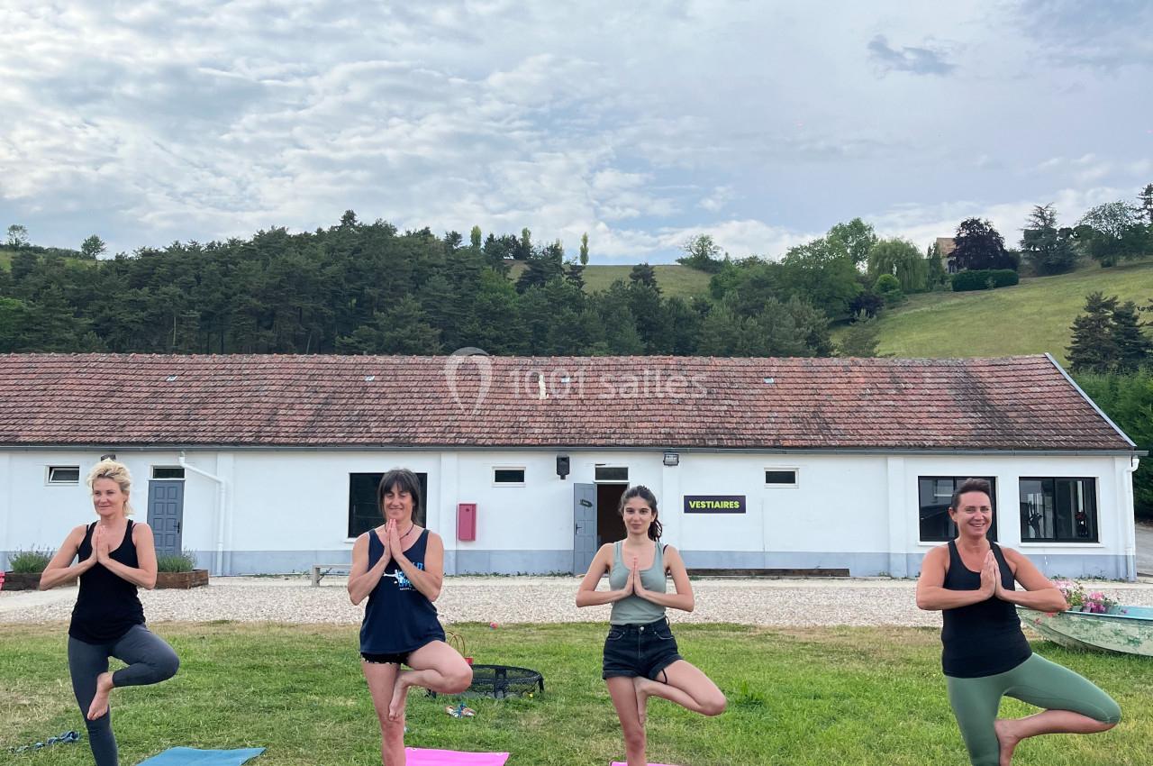 Quatre femmes pratiquant le yoga en posture de l'arbre sur des tapis colorés dans un espace extérieur herbeux.