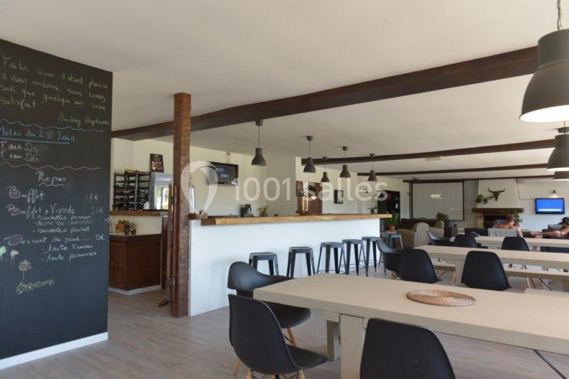 Salle de restaurant lumineuse avec tables en bois clair, chaises noires, bar en bois et tableau noir avec menu écrit à la…