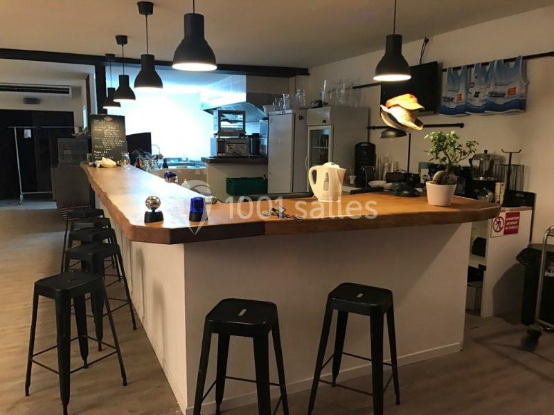 Un comptoir en bois entouré de tabourets noirs dans un espace de cuisine ou bar moderne et éclairé.