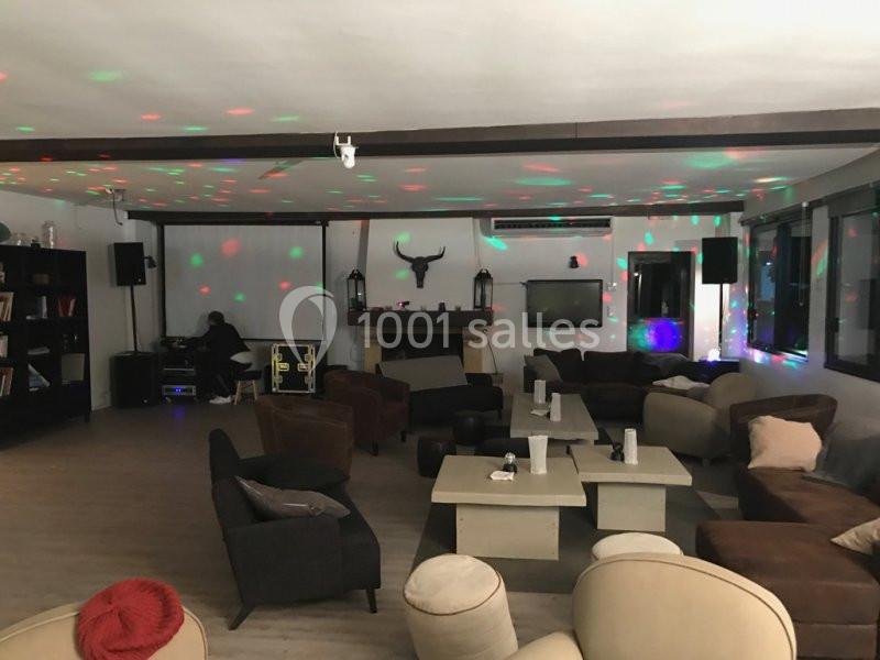 Salle de détente avec fauteuils, tables basses et éclairage coloré, décorée d'une cheminée et d'étagères.