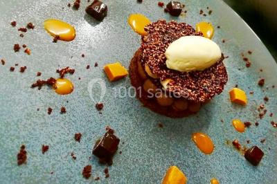 Salon d'hôtel avec canapés beiges, table basse, bureau, chaise noire et grande baie vitrée donnant sur un jardin.