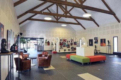 Salon d'hôtel avec canapés beiges, table basse, bureau, chaise noire et grande baie vitrée donnant sur un jardin.