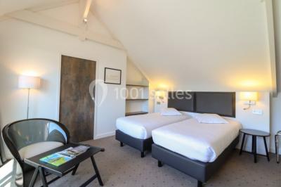 Salon d'hôtel avec canapés beiges, table basse, bureau, chaise noire et grande baie vitrée donnant sur un jardin.