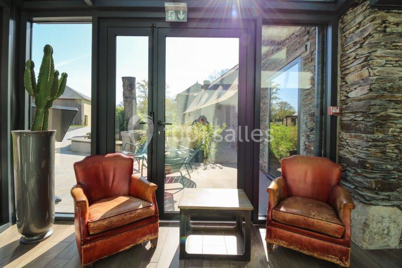 Deux fauteuils en cuir rouge encadrent une petite table devant une baie vitrée donnant sur une terrasse ensoleillée.