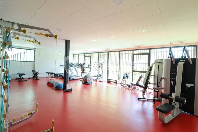 Salle de sport lumineuse avec équipements de musculation, tapis de course et machines de fitness sur un sol rouge.