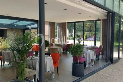 Salon d'hôtel avec canapés beiges, table basse, bureau, chaise noire et grande baie vitrée donnant sur un jardin.
