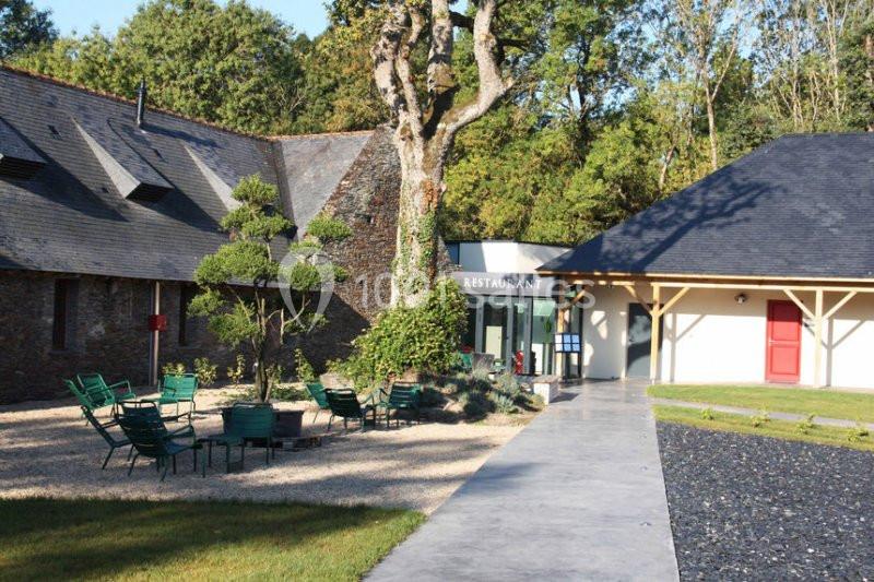 Cour extérieure avec des chaises vertes autour d'une table, entourée de bâtiments en pierre et en bois, près d'un arbre.