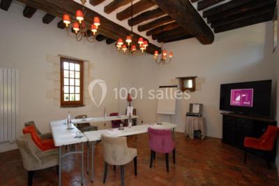 Salon d'hôtel avec canapés beiges, table basse, bureau, chaise noire et grande baie vitrée donnant sur un jardin.