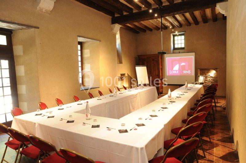 Salle de réunion lumineuse avec tables disposées en U, chaises rouges et écran de projection allumé.