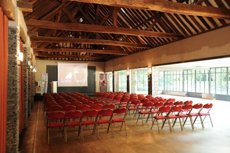 Salle de séminaire avec rangées de chaises rouges, écran de projection et poutres apparentes en bois.