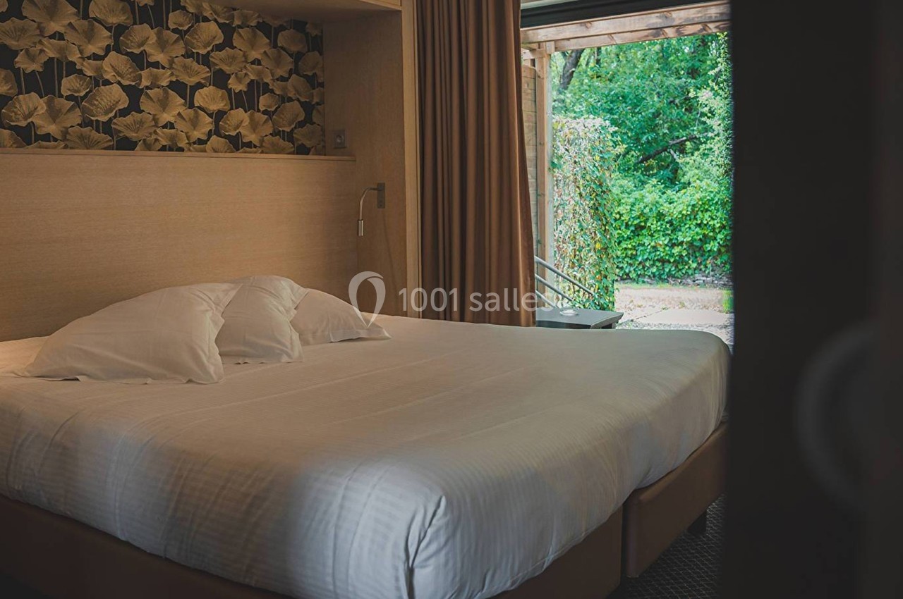 Lit double avec draps blancs dans une chambre au décor chaleureux, vue sur un jardin verdoyant par une porte ouverte.